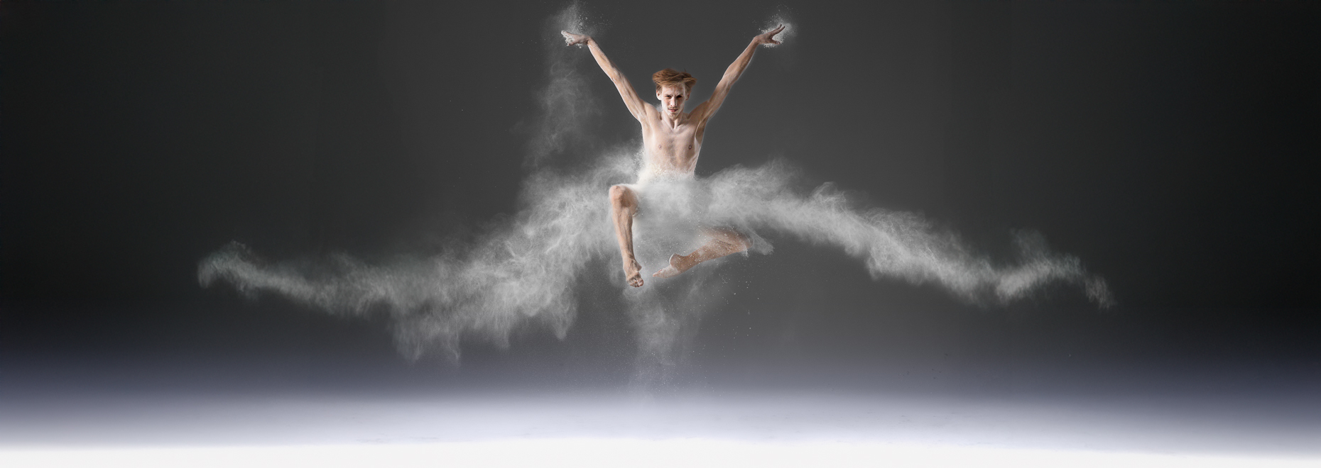 Moderner T&auml;nzer springt kraftvoll auf einer professionellen Tanzfl&auml;che, Staub hebt Dynamik und Bodenhaftung hervor